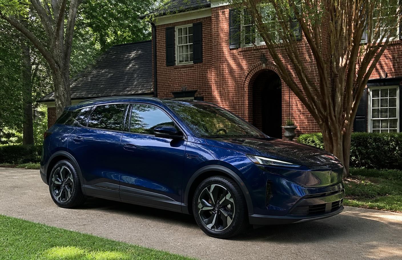Glossy dark blue electric SUV parked in a tree-shaded suburban brick-home driveway