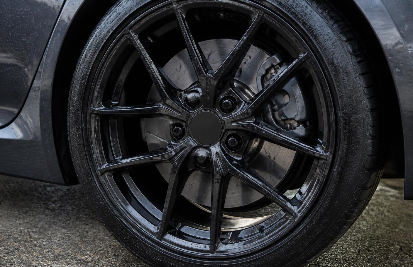 Close-up of a clean gloss black alloy wheel with water beading on the wheel face