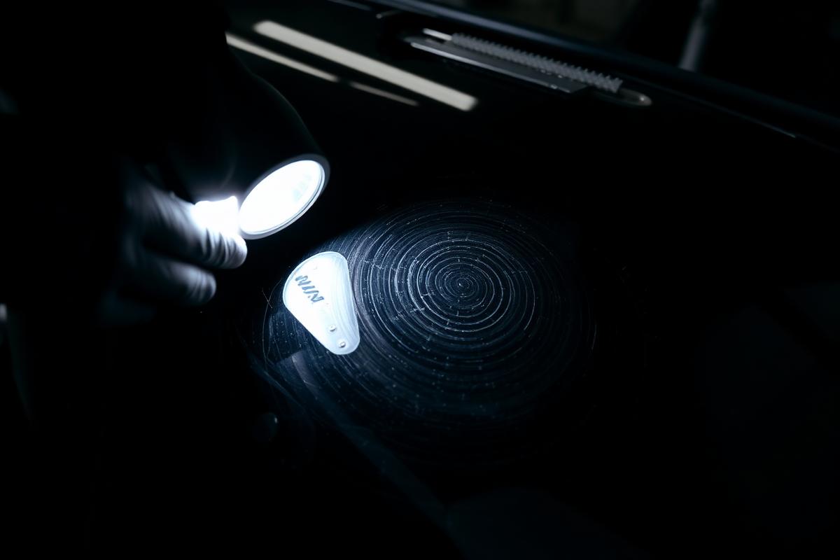 Detailer inspecting swirl marks on dark car paint under a focused inspection light